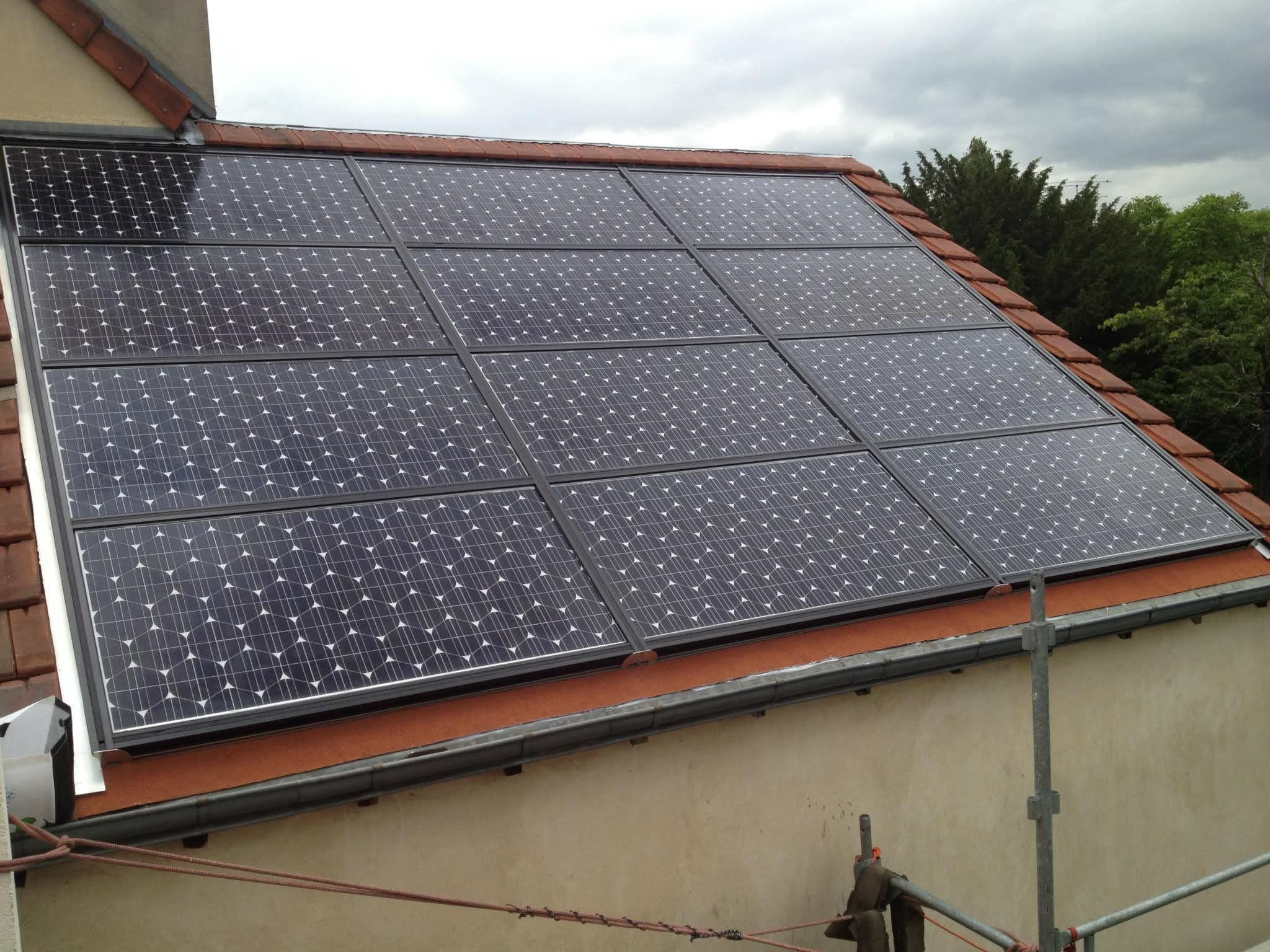 Douze panneaux solaires alignés en trois rangées sur un pan de toiture en tuiles, vus de trois quarts depuis l’échafaudage.