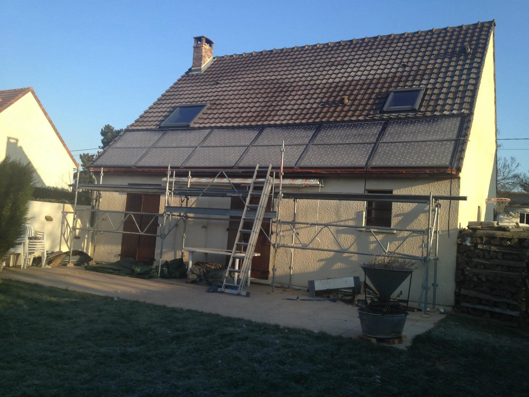 Pavillon en fin de chantier : un pan entier de toiture couvert de panneaux solaires, échafaudage encore en place le long de la façade, gelée blanche sur la pelouse.