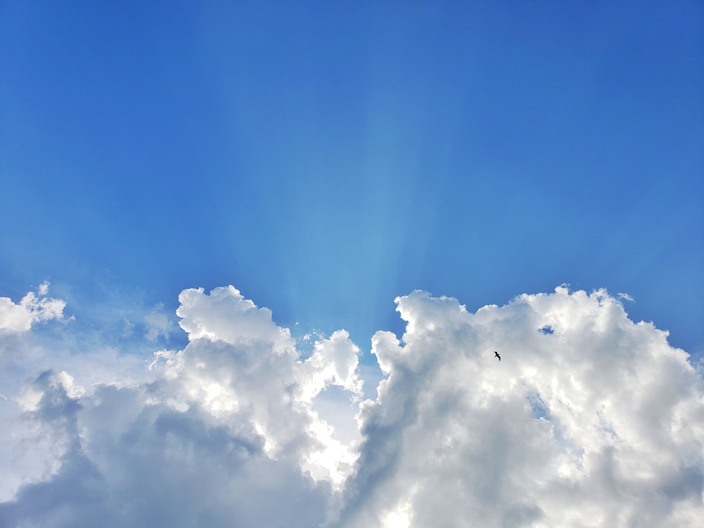 Ciel bleu avec de grands nuages blancs et des rayons de soleil perçant entre eux.