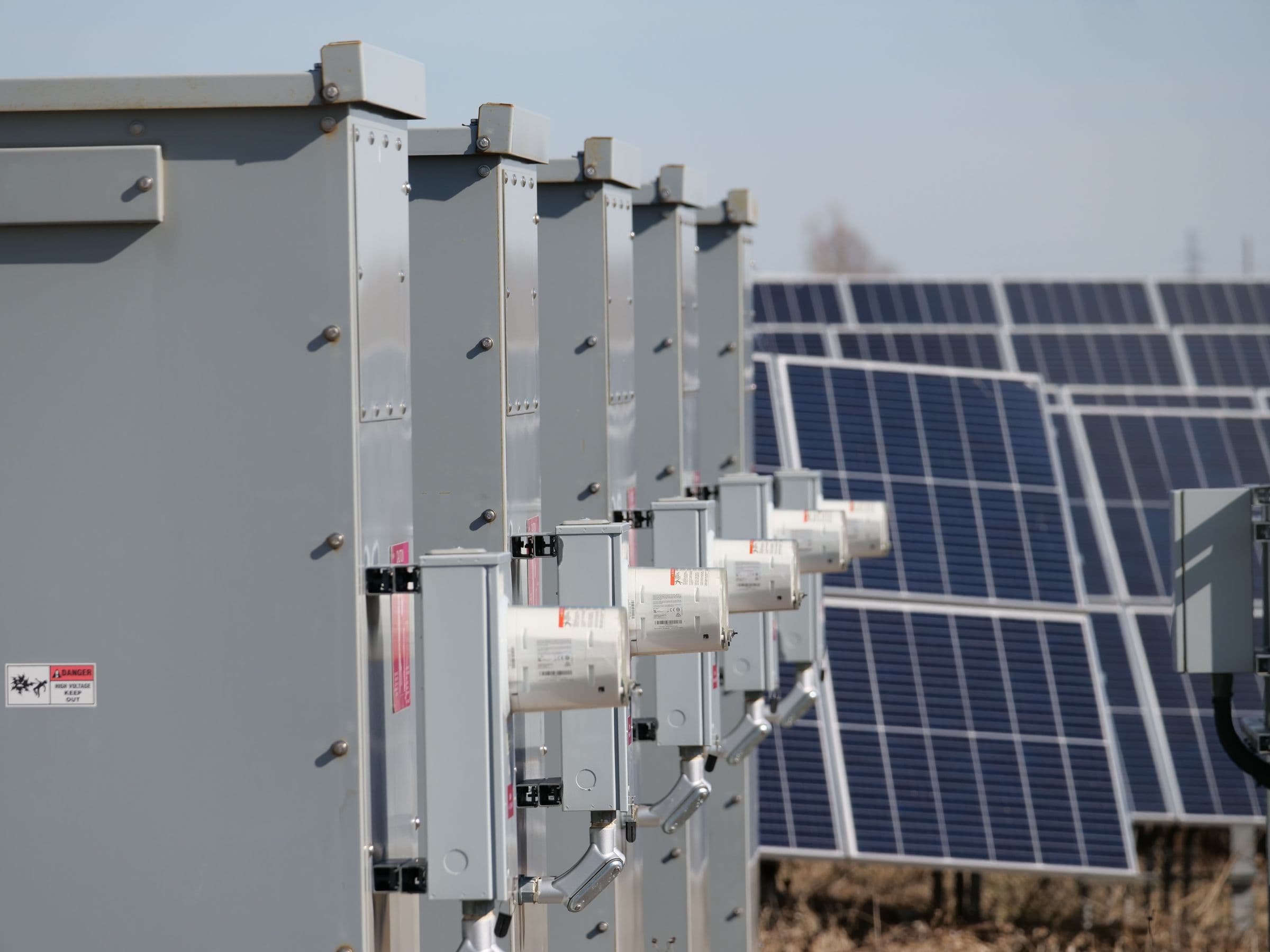 Rangée de coffrets électriques de raccordement montés sur une structure métallique, panneaux solaires en arrière-plan.