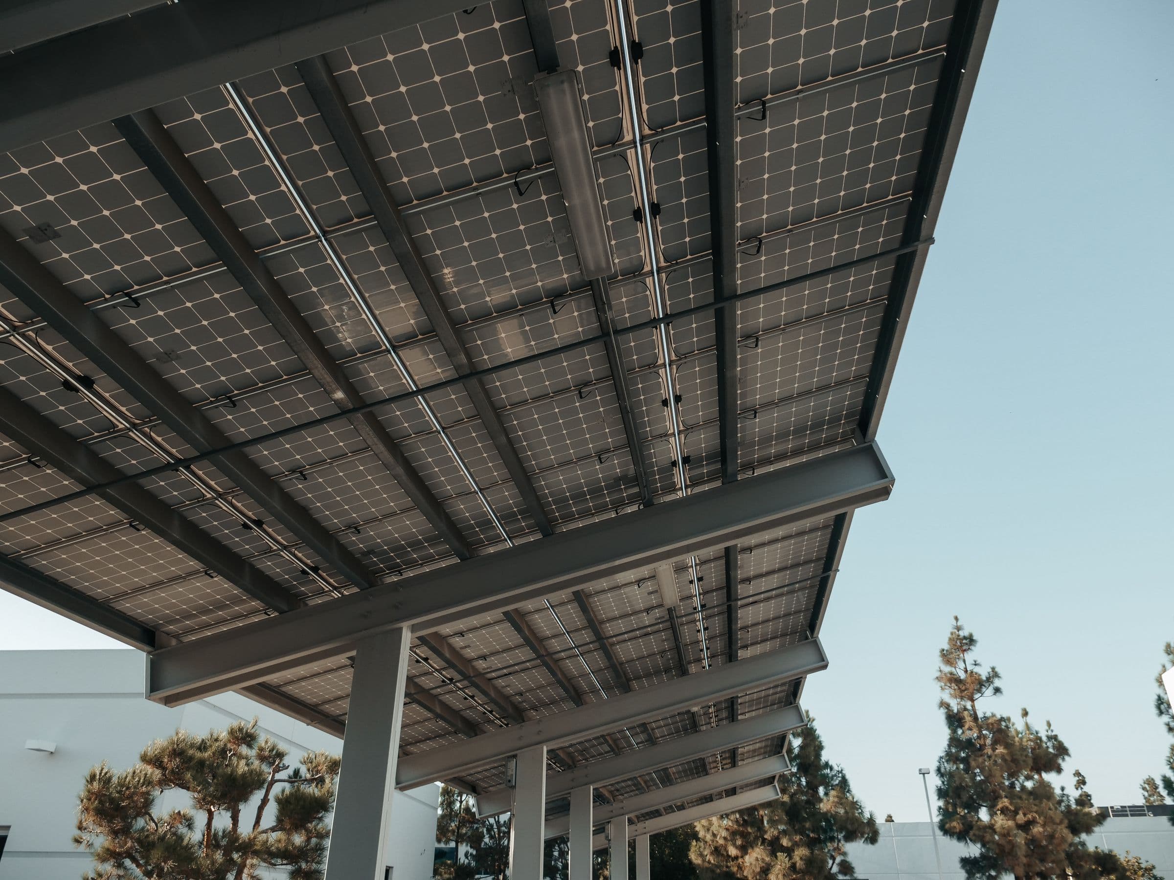 Vue en contre-plongée sous une ombrière solaire de parking, structure métallique et panneaux photovoltaïques.