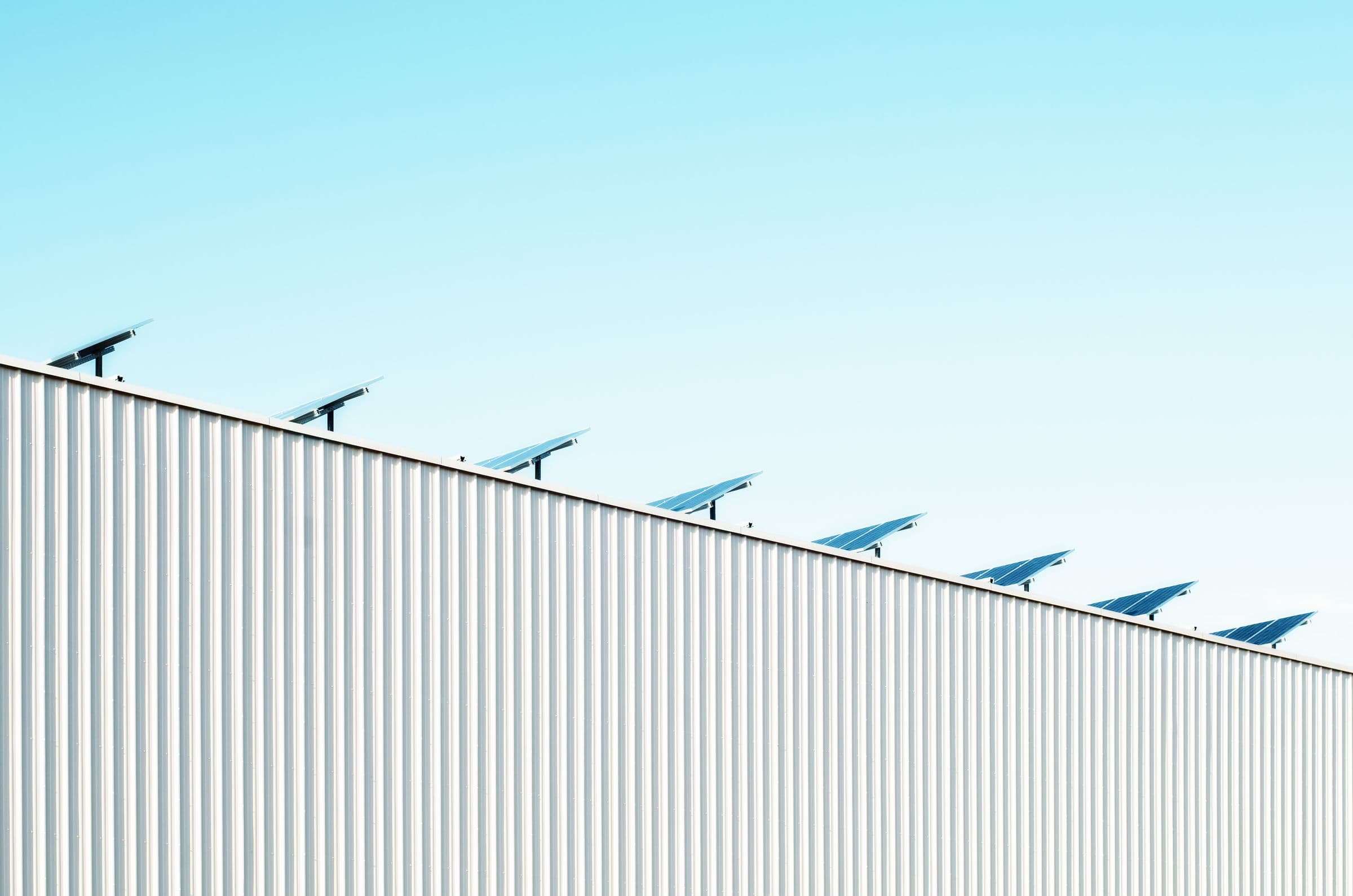 Panneaux solaires inclinés en crête du toit métallique d’un hangar, ciel dégradé épuré.