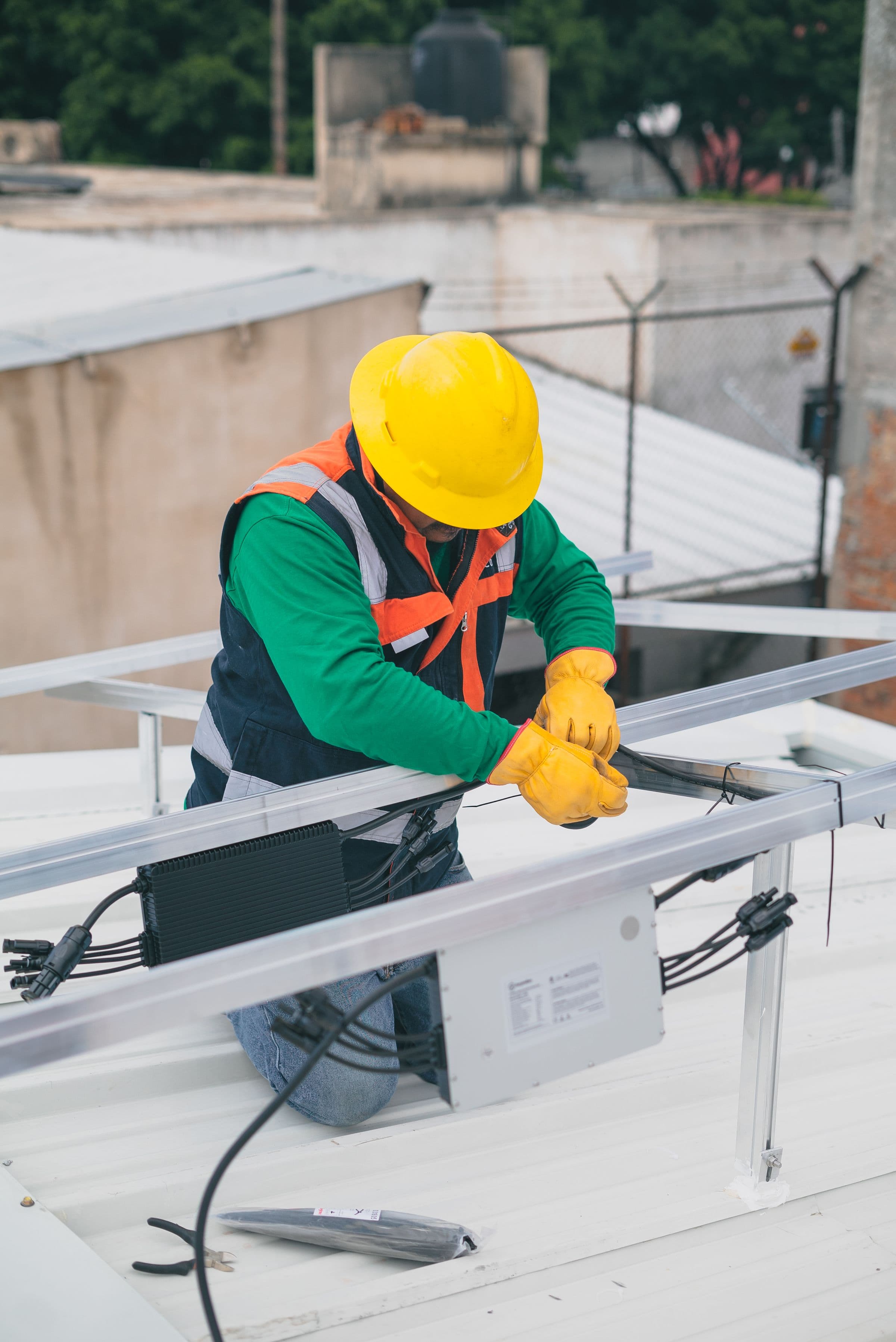 Technicien agenouillé sur une toiture équipée de panneaux solaires, intervenant sur le boîtier de jonction et son câblage.